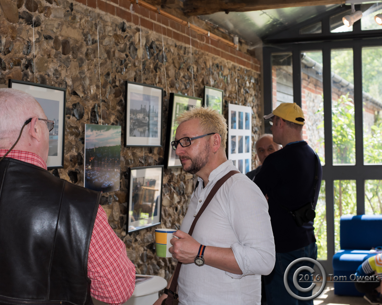 man with mug of tea listens to another man, two men in background