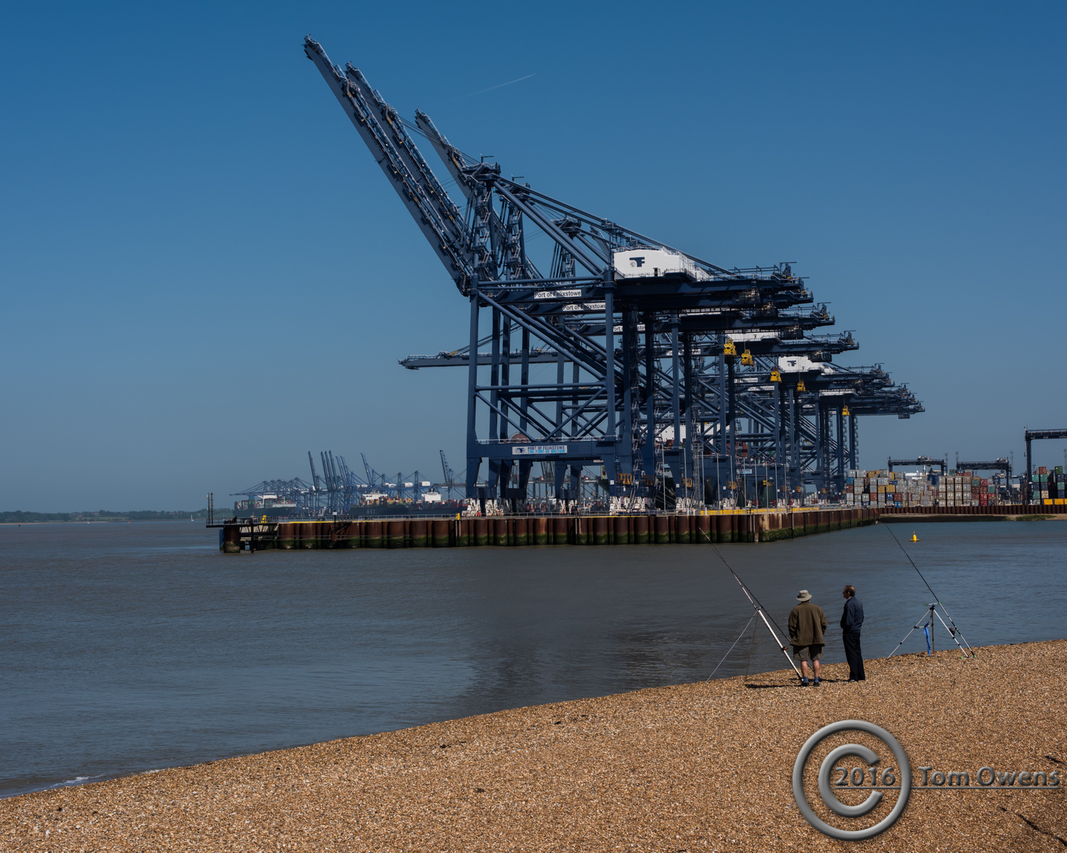 Two fishermen on shingle with cranes in background